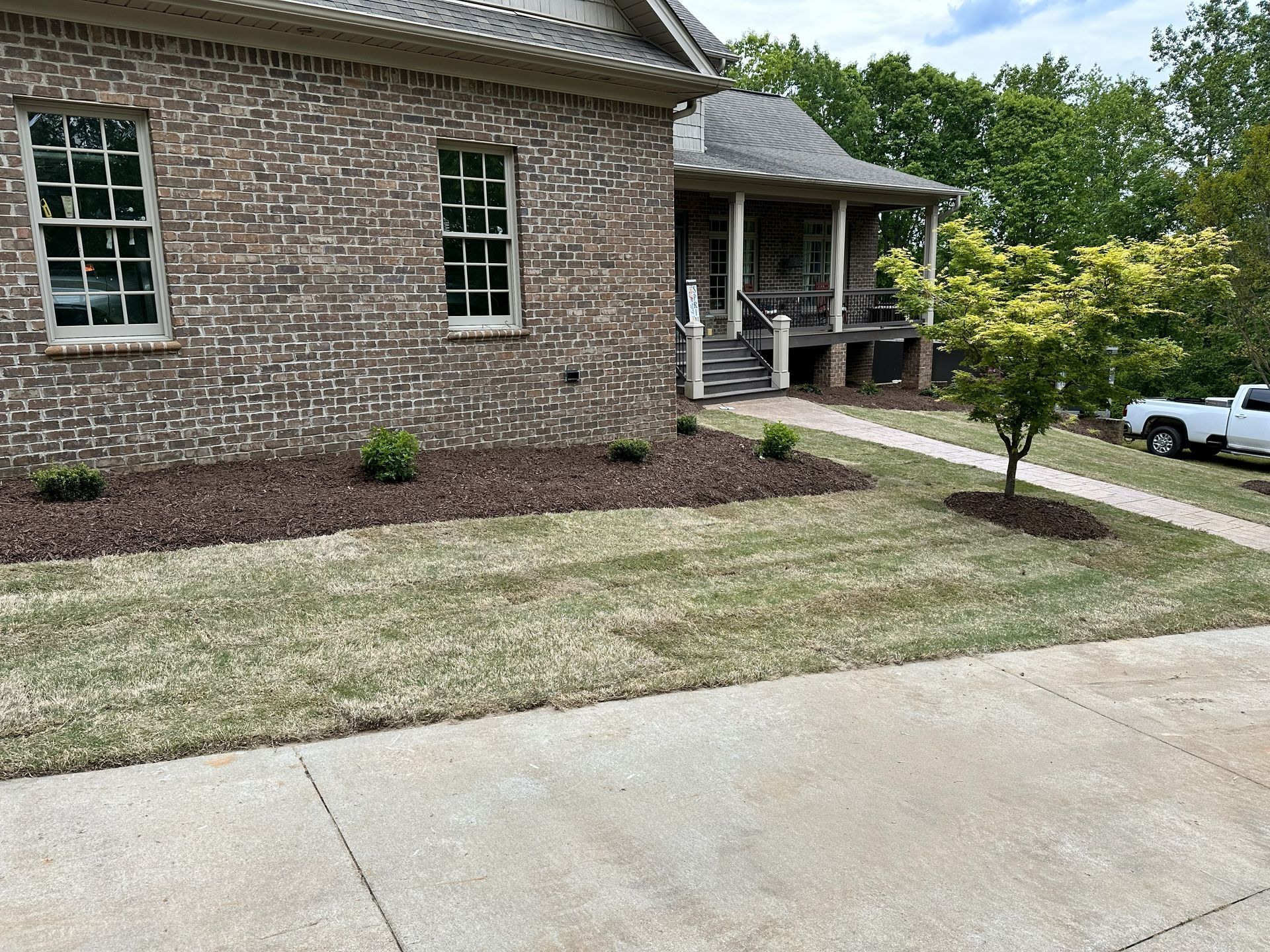 Brick house with lawn and landscaped beds. Walkway to porch.  White truck parked nearby.