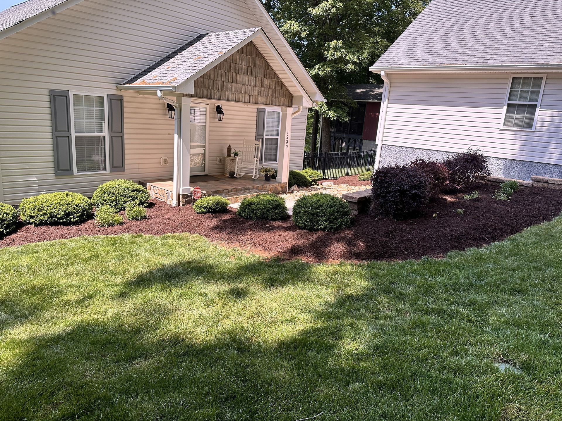 A house with a porch and a detached building. Landscaped area with shrubs and mulch. Green grass in foreground.