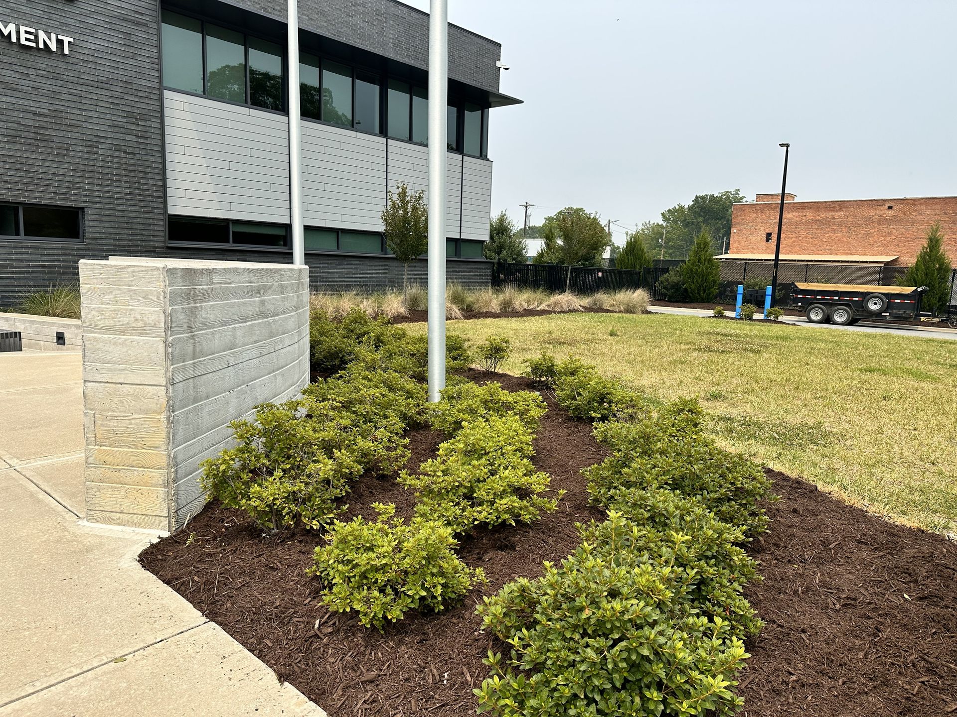 Building exterior with landscaping, flagpoles, and shrubs. Brown mulch and green grass.