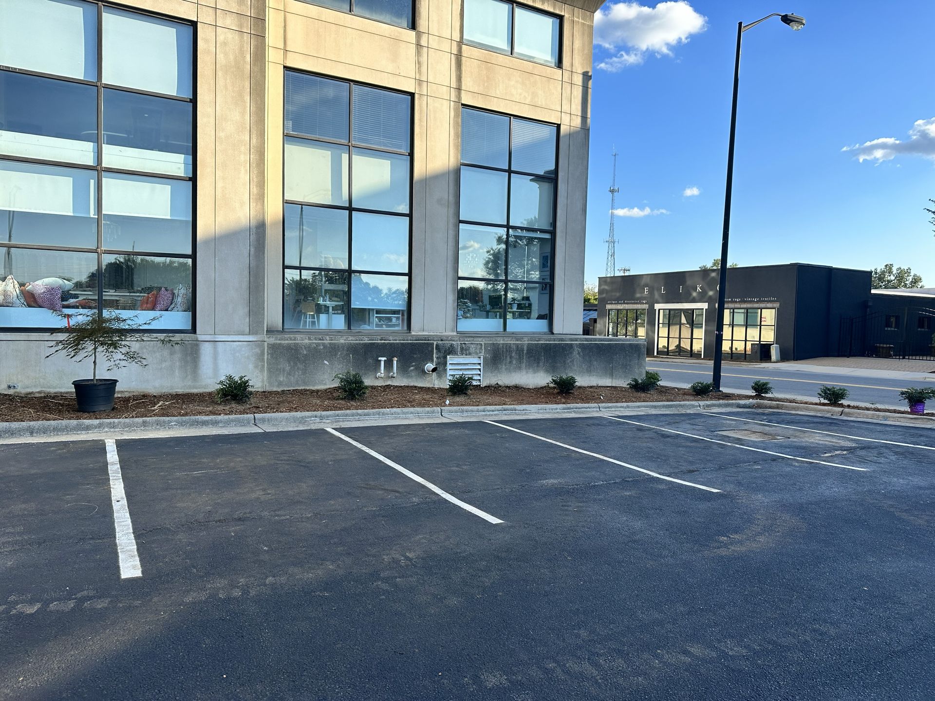 A new asphalt parking lot with white lines in front of a modern building with large windows.