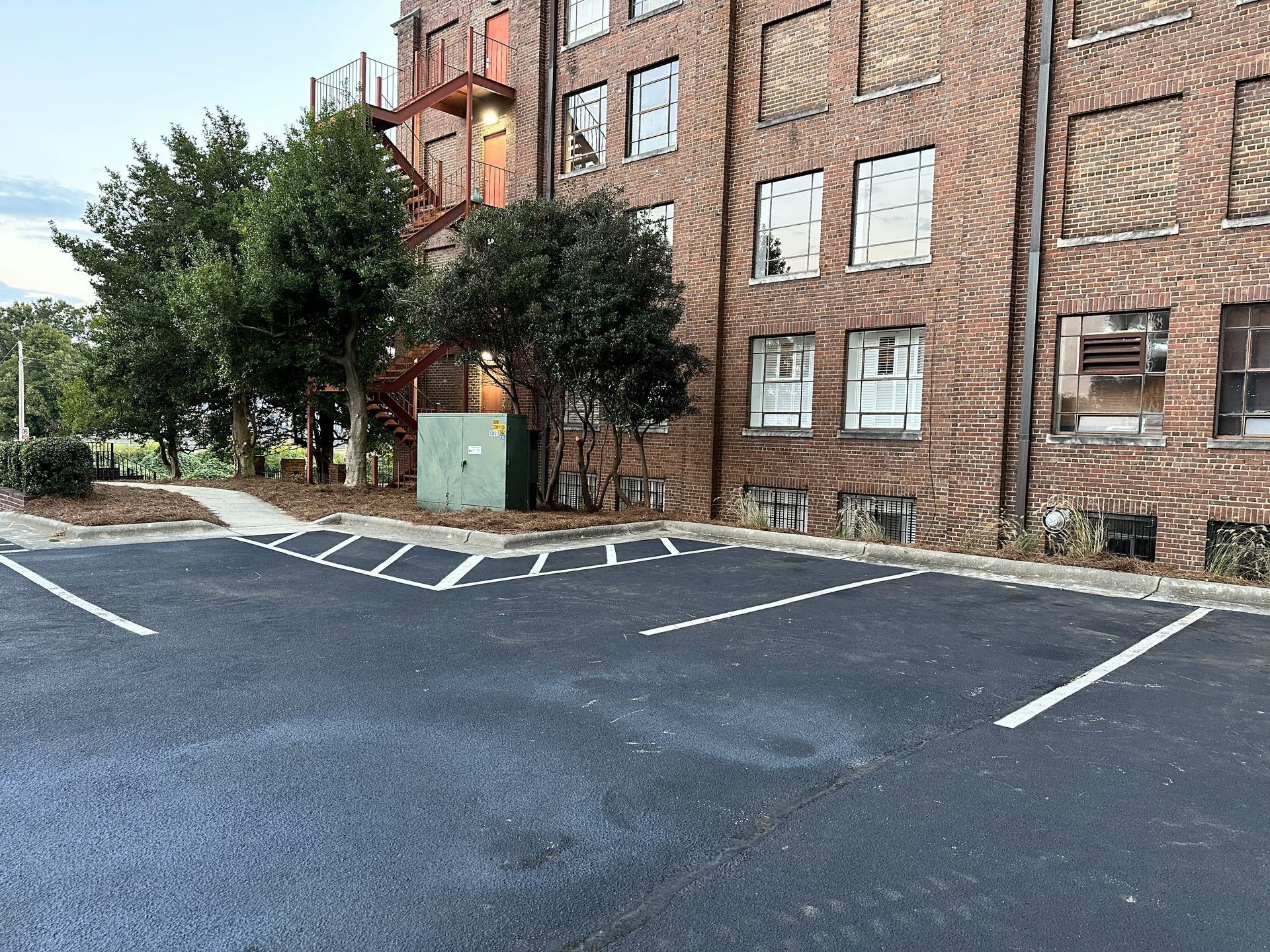 Parking lot in front of a brick building with boarded windows and a red fire escape.