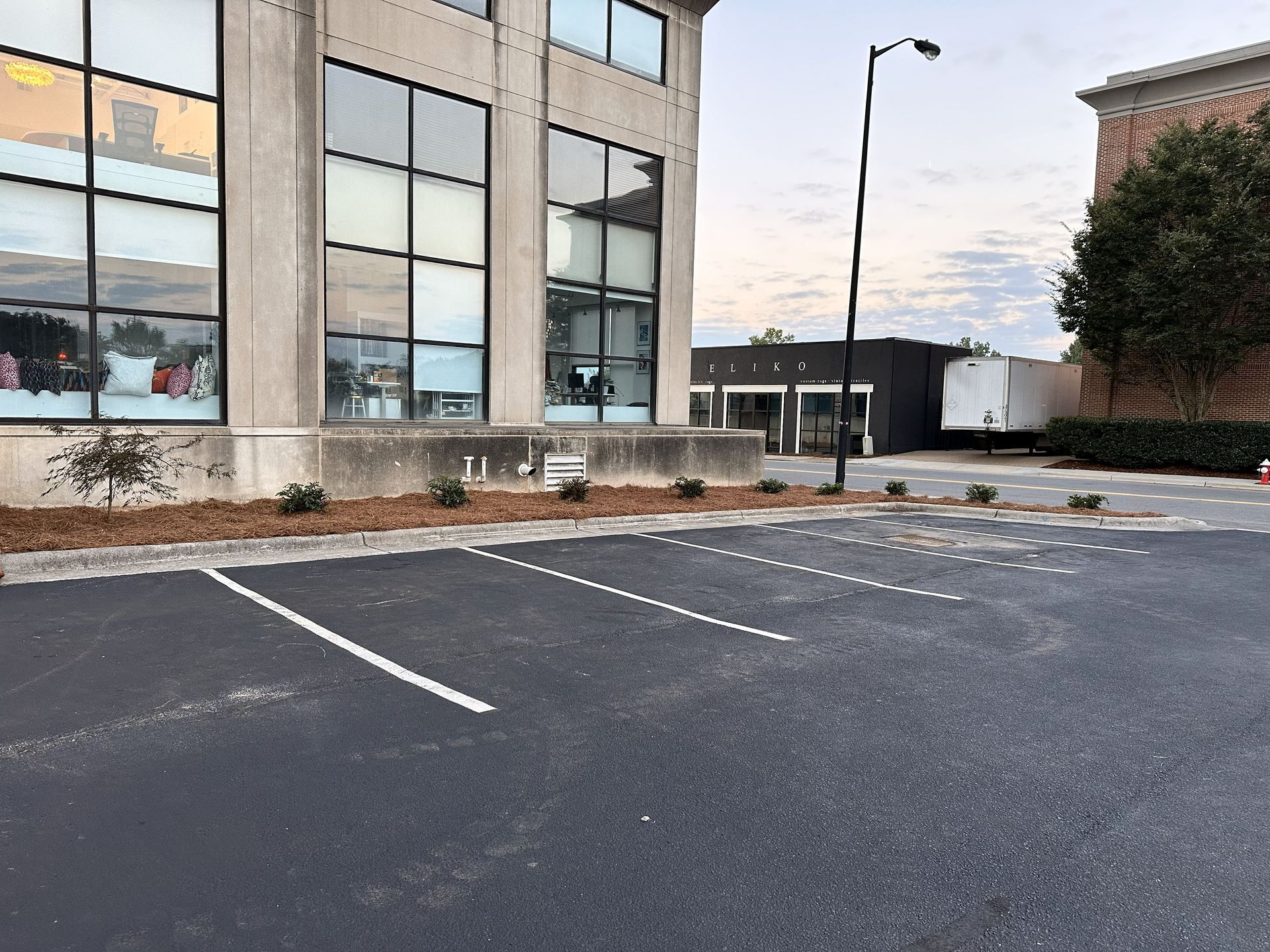 Empty parking lot in front of a concrete building with large windows.