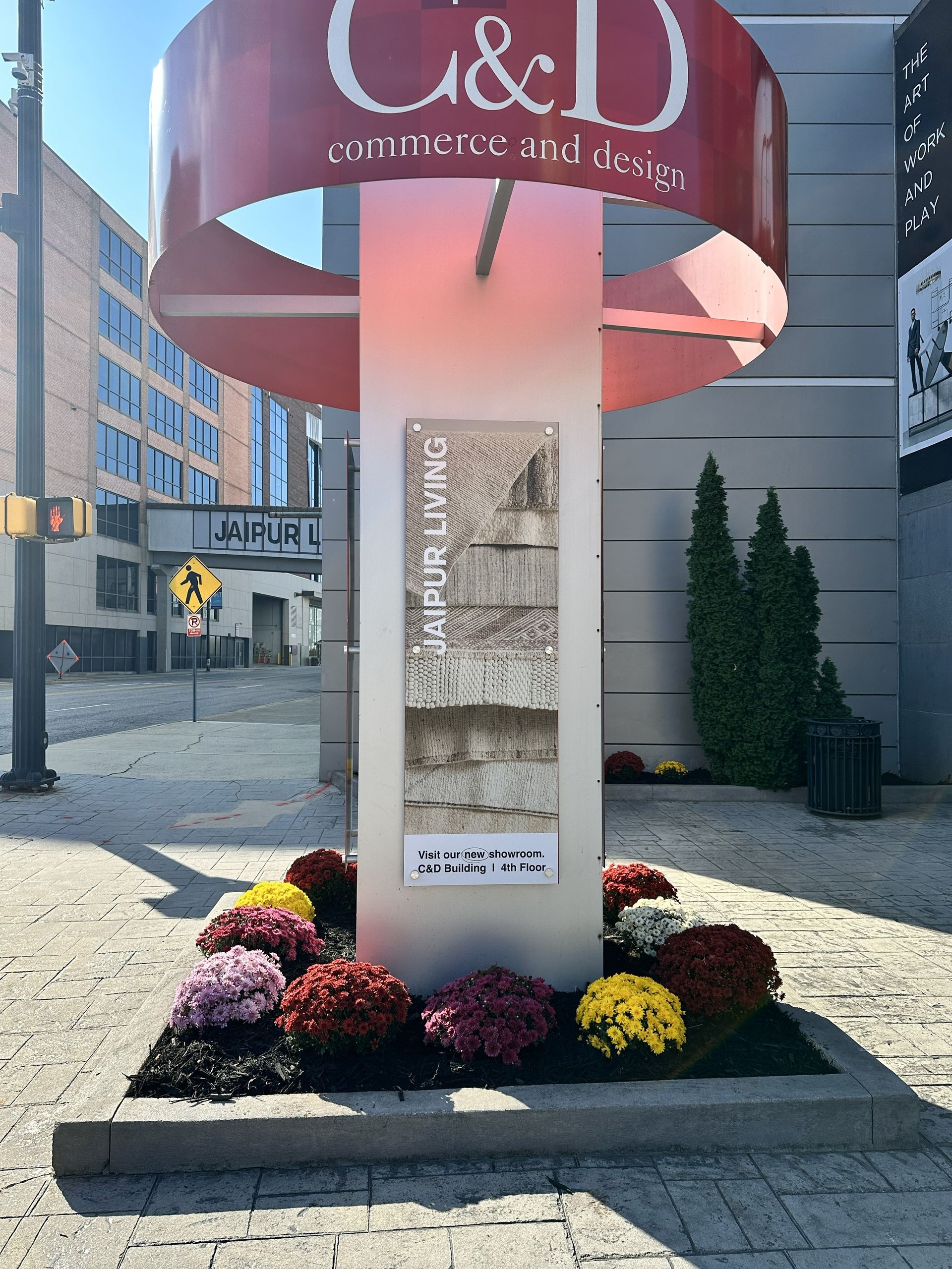 Sign for C & D Commerce and Design with red accents, a central display, and colorful flowers at its base.