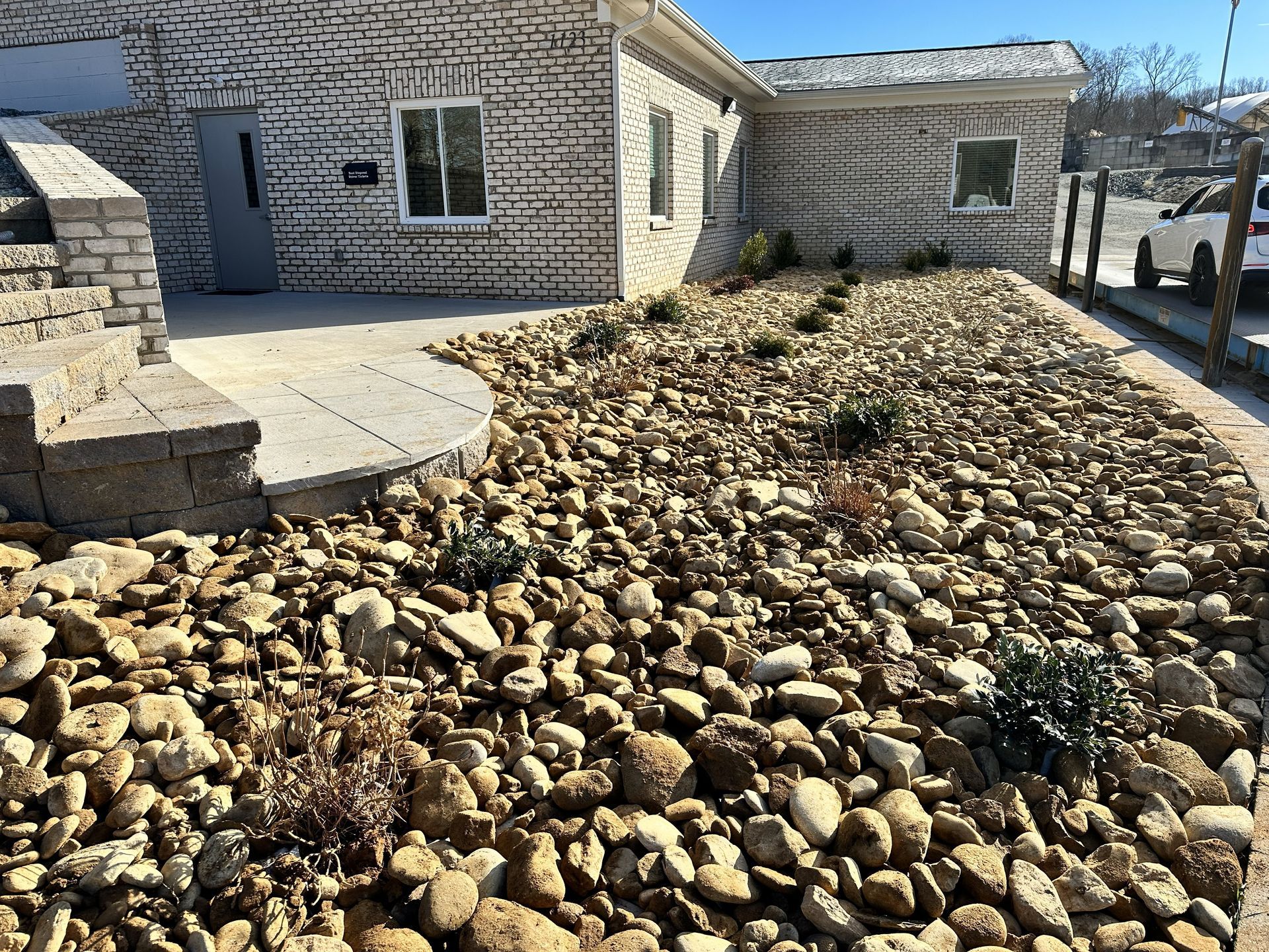 Exterior of a light brick building with a rock garden in front. Sunny day.