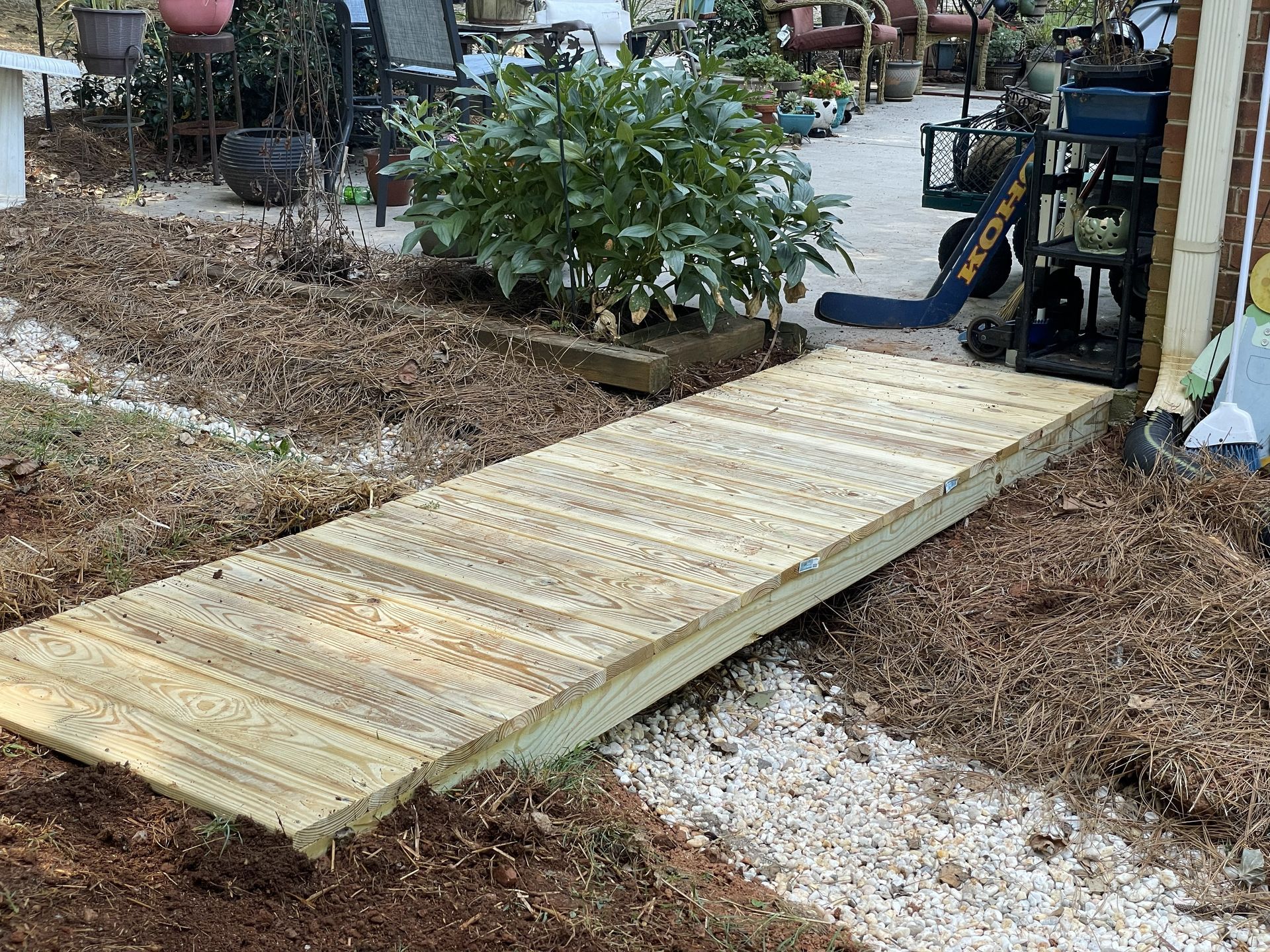 Wooden ramp leading to a building entrance, set on mulch and gravel, in an outdoor setting.
