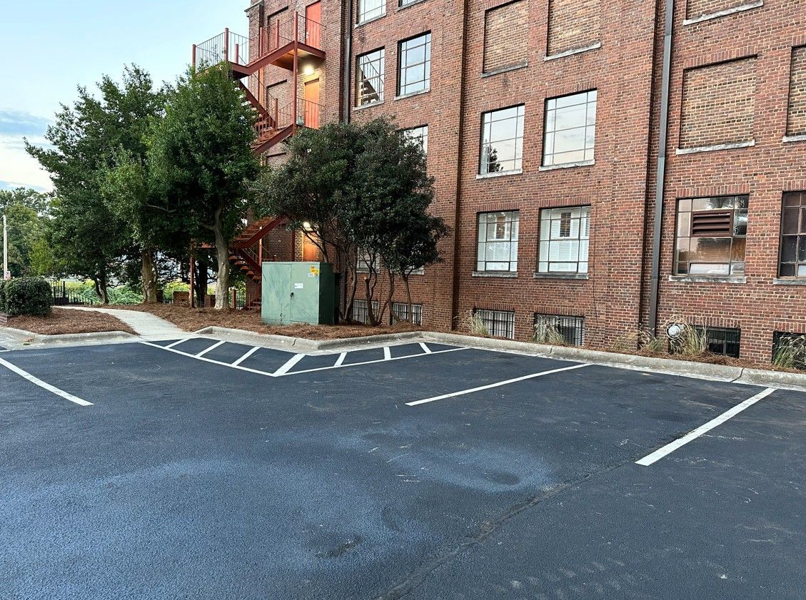 Parking lot with painted lines in front of a brick building and trees.