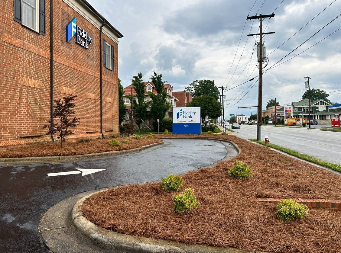 Brick building with a blue sign. Mulched landscaping borders a curved driveway along a road. Cloudy sky.