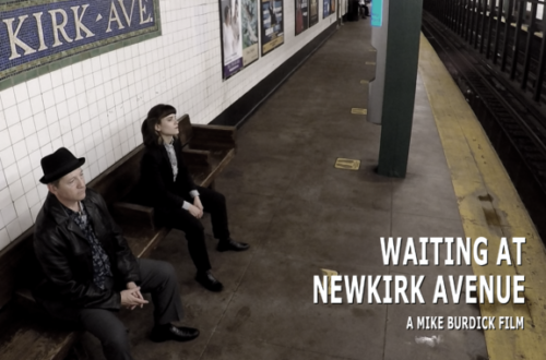 Two people sit on a subway platform beneath a KIRK AVE sign, waiting at Newkirk Avenue.
