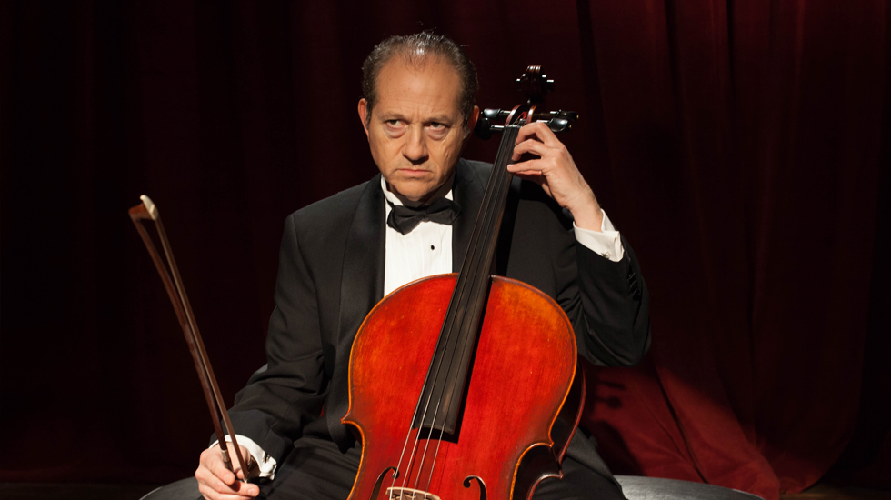 Cellist in a tuxedo playing a cello on a stage with red curtains