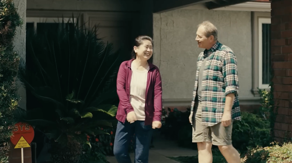 Two people talking outside a house, smiling in front of the front porch.