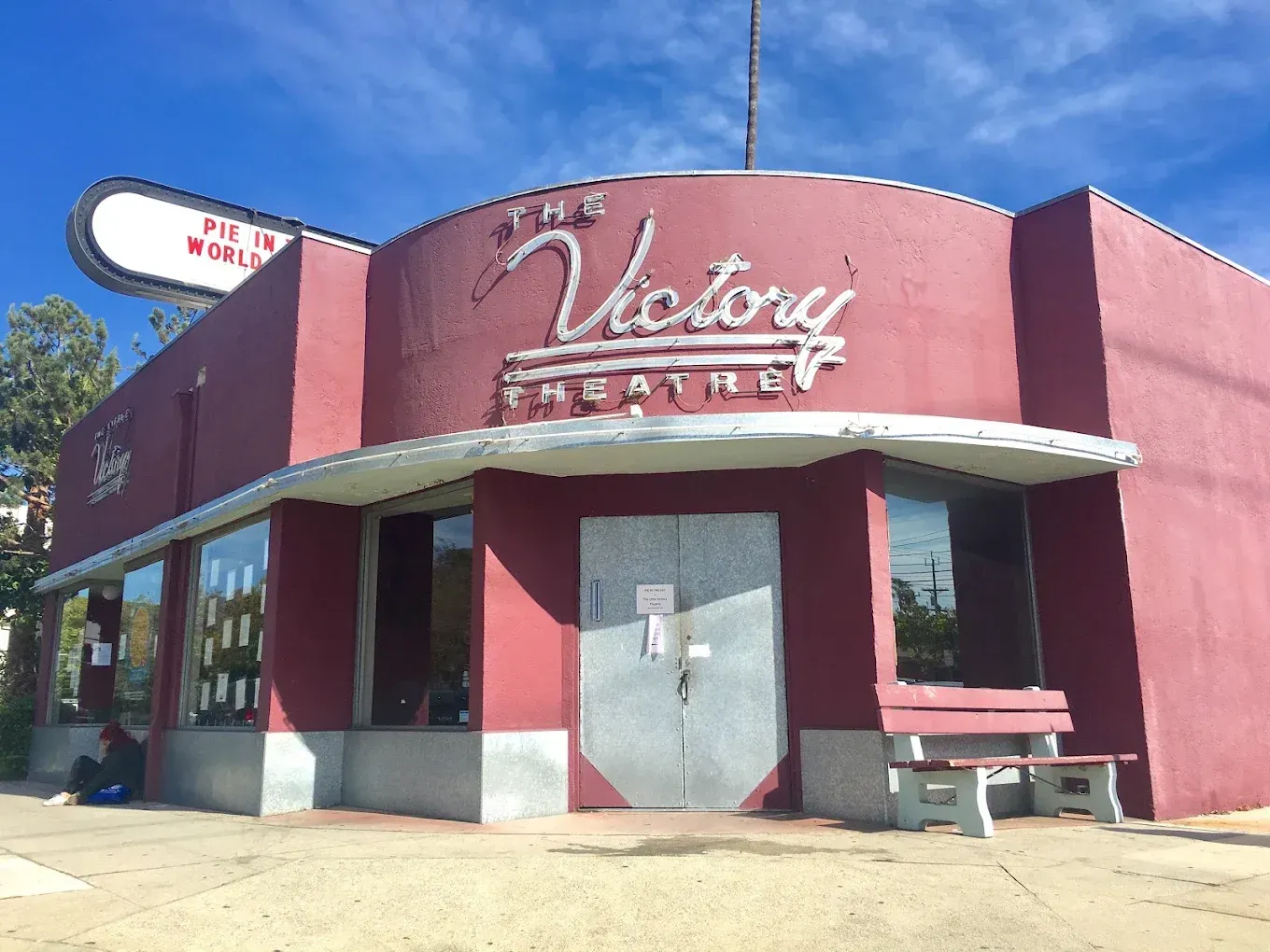 Red storefront with white awning and sign reading “Victory Theater” under a blue sky