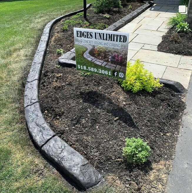a sign for edges unlimited is sitting in the middle of a garden .