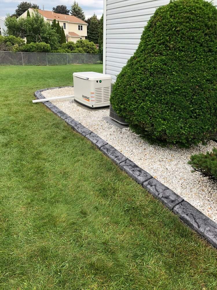 a generator is sitting on the side of a lush green lawn next to a house .