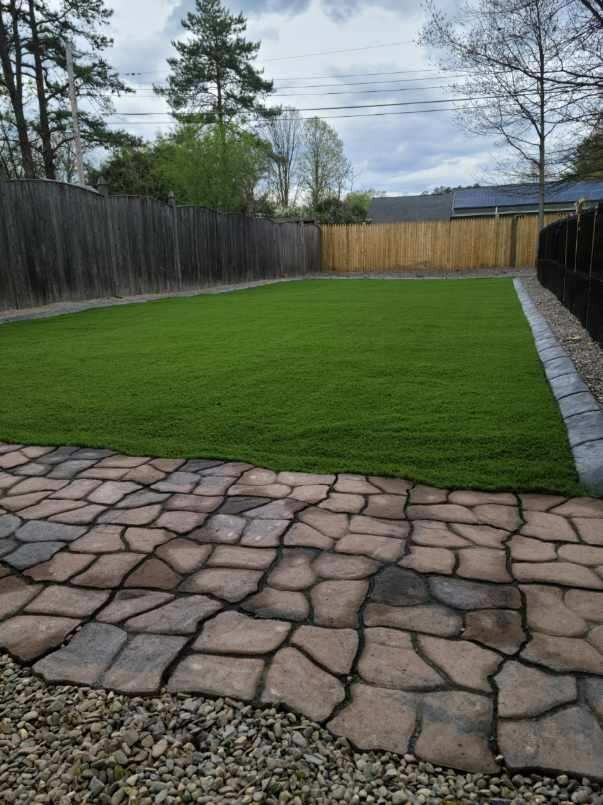 a backyard with a brick walkway and a lush green lawn .
