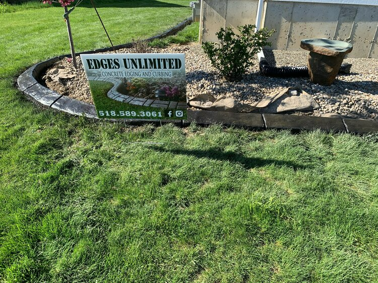 a sign for edges unlimited is sitting in the middle of a lush green lawn .