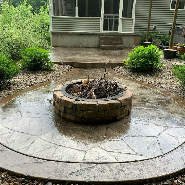 a fire pit is sitting on a concrete patio in front of a house .