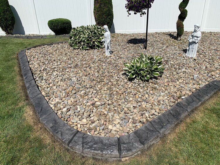 a gravel garden with a concrete border and a white fence in the background