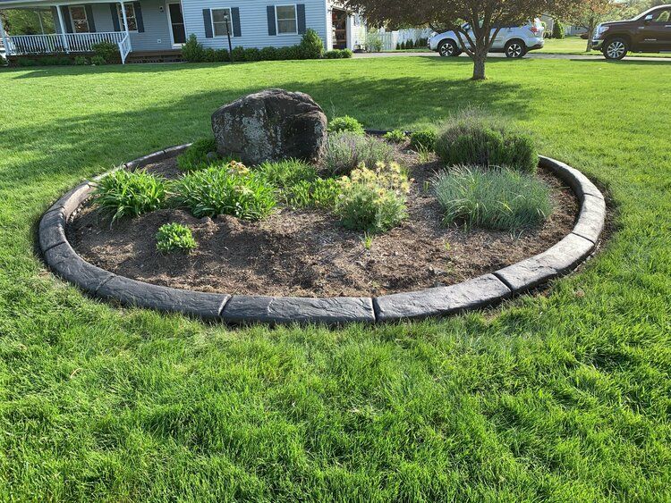 a circular garden in the middle of a lush green lawn in front of a house