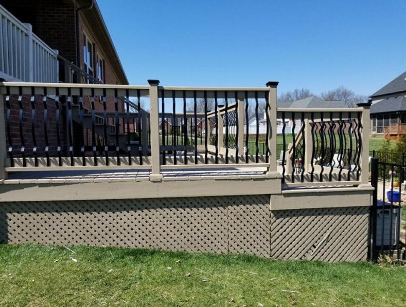 Tan deck with decorative black railing, lattice siding, and green grass against a blue sky.