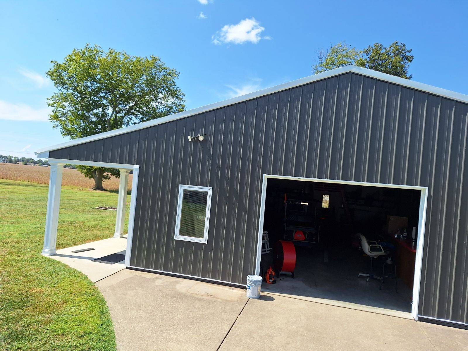 Gray metal shed with open garage door, white trim, and a porch.