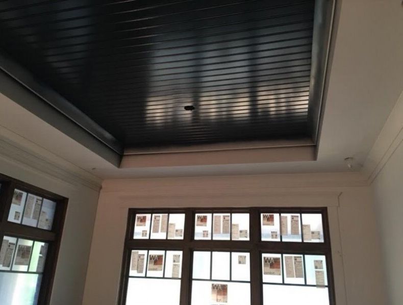 Ceiling with dark wooden slats, above white walls and windows with rectangular panes.