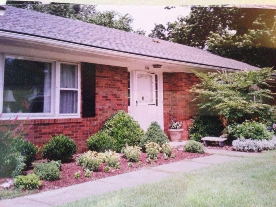 Brick ranch-style house with manicured landscaping, white door, and windows.