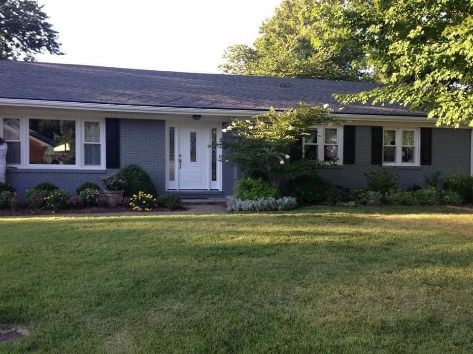 Gray brick ranch house with white trim, black shutters, and manicured landscaping.
