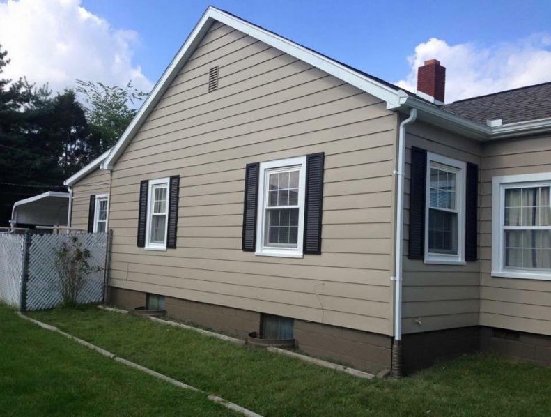 Beige house with black shutters, white trim, and a red brick chimney on a green lawn.