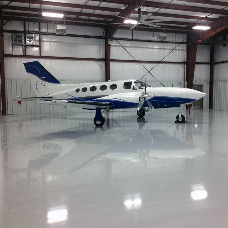 A small white and blue airplane inside a hangar with a reflective gray floor.