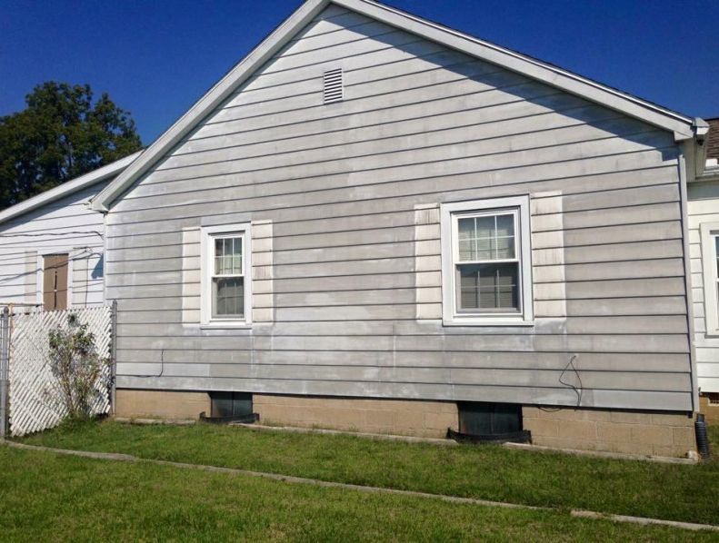 Gray siding house with two windows, white shutters, and a green lawn.