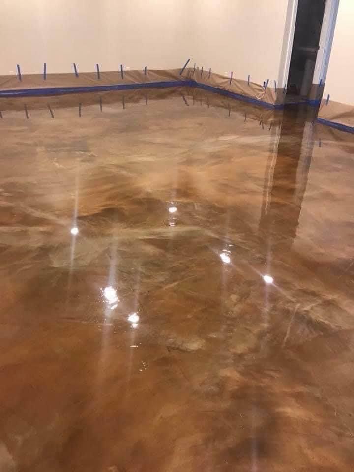 Metallic copper-colored epoxy floor with light reflections, corner with blue tape and small stakes.