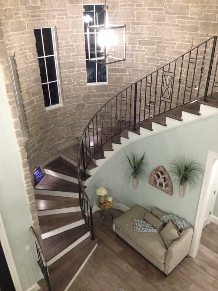 Stone turret stairway with wrought-iron railing, wooden steps, and light-blue walls. A small sofa sits beneath the stairs.