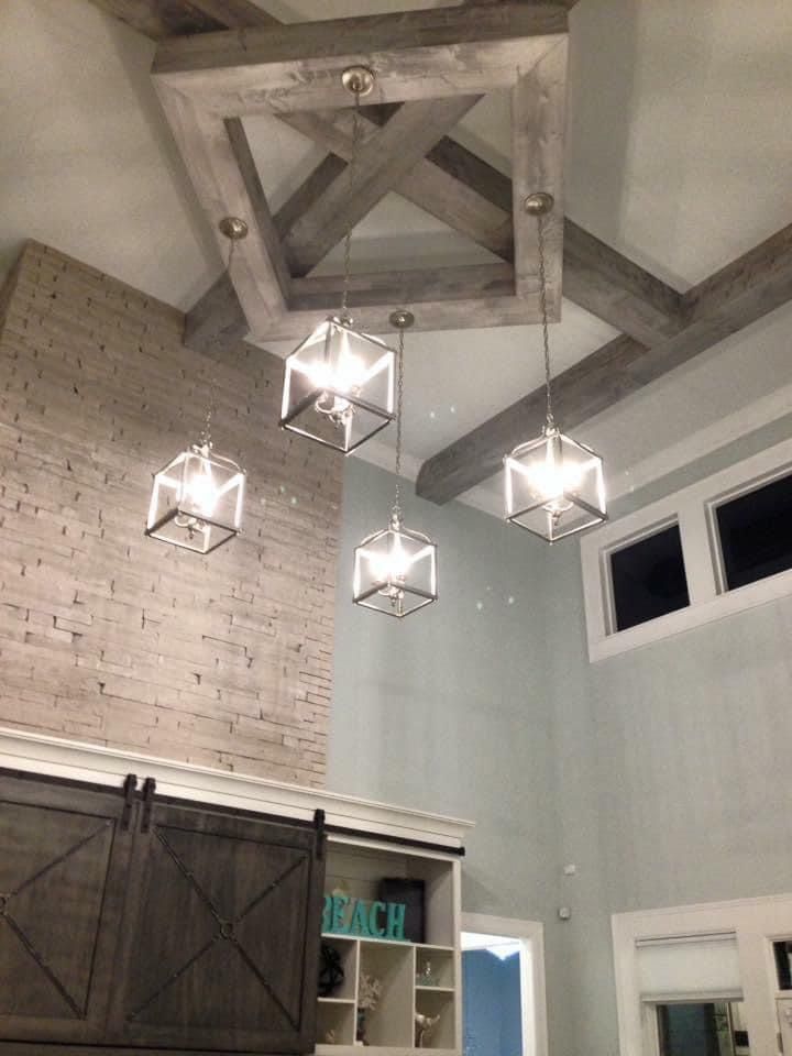 Four modern cube pendant lights suspended from a gray wooden ceiling fixture. A brick wall and barn door are visible.