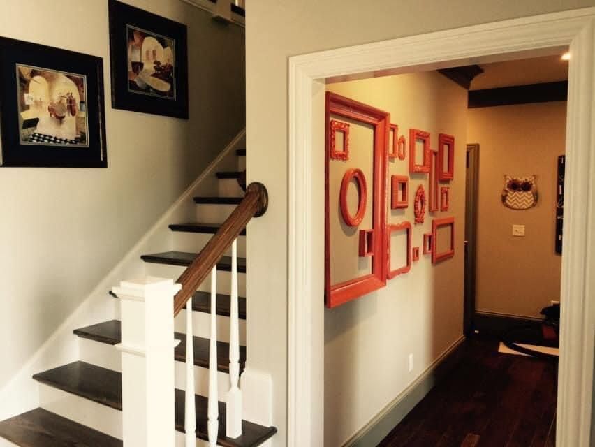 Hallway with stairs and decorative picture frames on the wall. Brown, white, and orange accents.