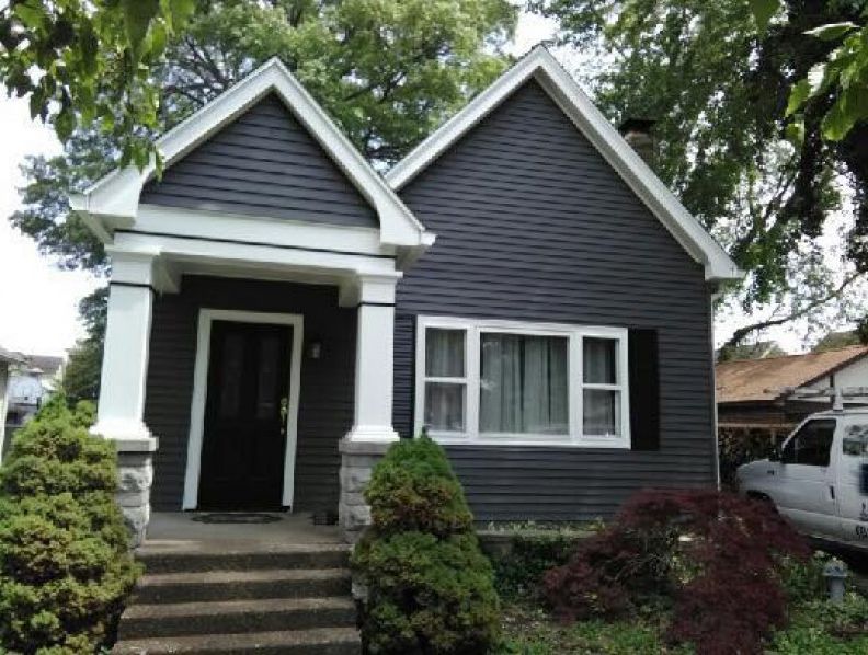 Dark gray house with white trim, porch, and steps; bushes in the yard.