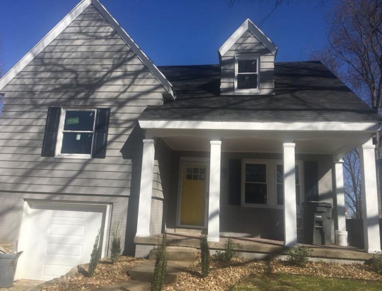 Gray house with yellow door, white pillars, black shutters, and two gable dormers.