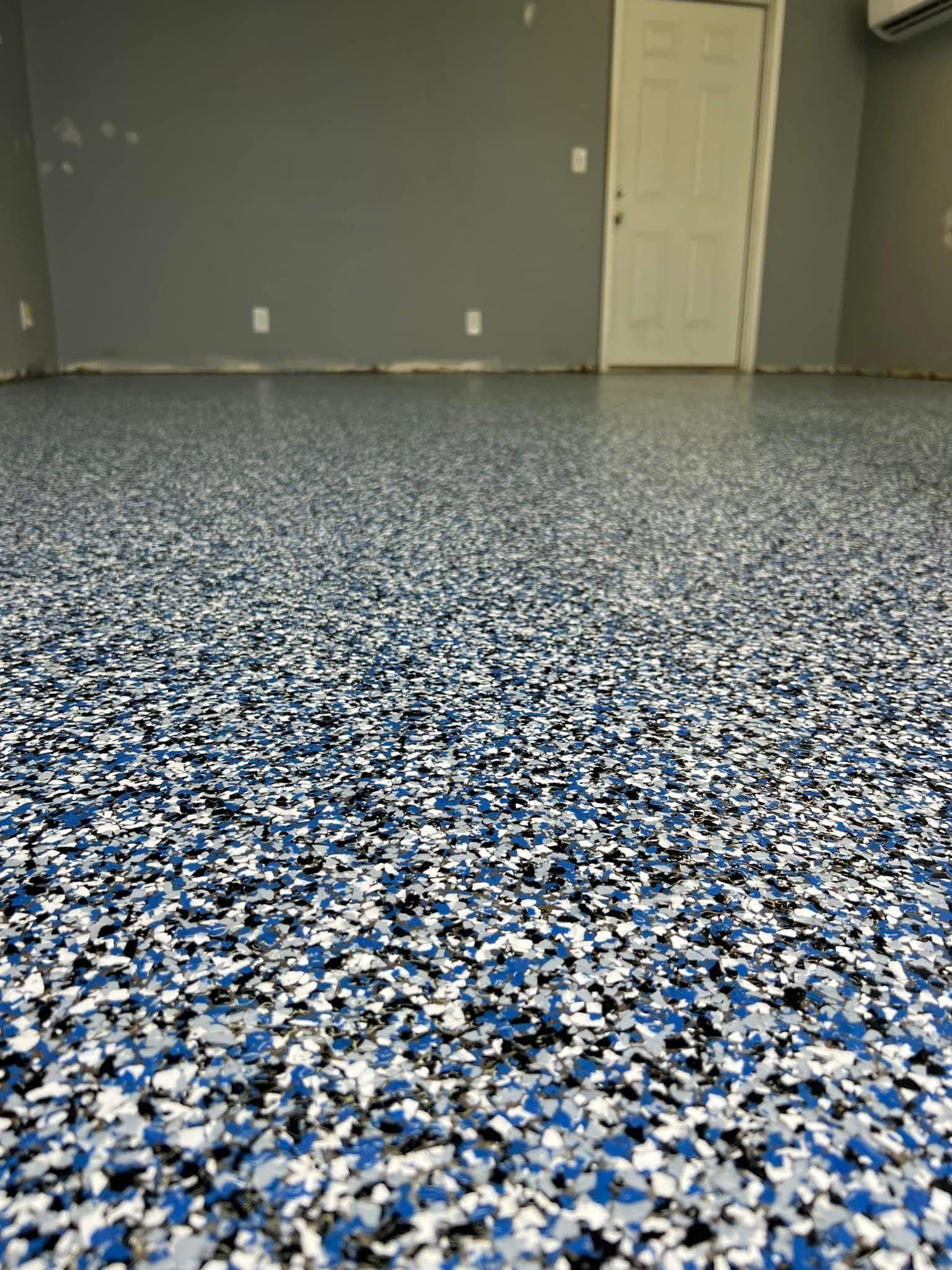 Epoxy garage floor with blue, black, and white chips. Gray walls, white door.