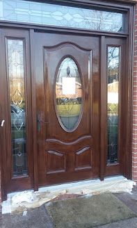 Brown wooden front door with sidelights and stained glass, beneath a transom window.