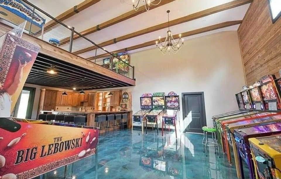 Game room with pinball machines, bar, and loft area; blue epoxy floor.