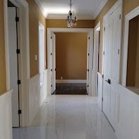 Hallway with white wainscoting and doors, glossy white floor, tan walls, and a chandelier.
