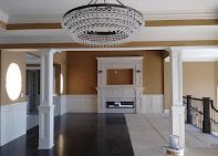 Elegant room with chandelier, fireplace, white columns, dark floor, and light walls.