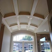Coffered ceiling with white beams, above arched window with outside view.