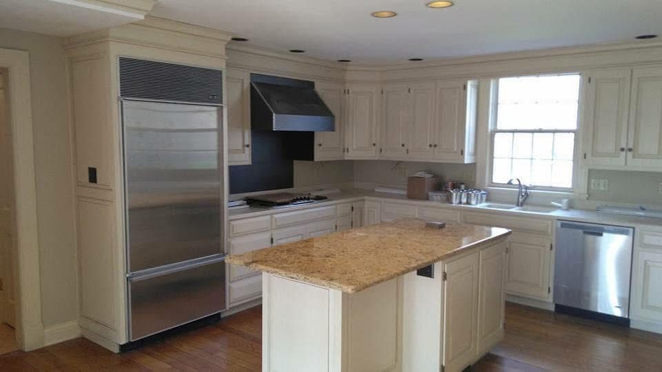 Cream-colored kitchen with a stainless steel refrigerator, island with granite countertop, and dishwasher.