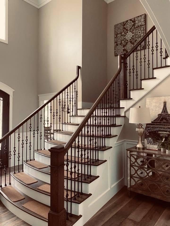 Two-story staircase with brown railing and balusters. Beige walls, wood flooring, and decor.