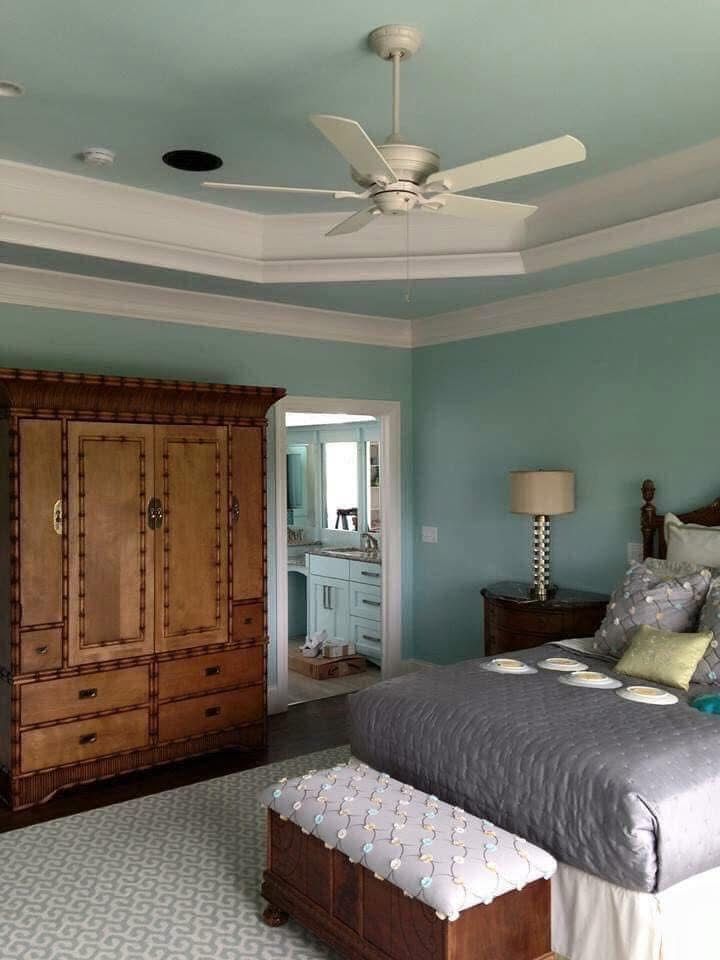 Bedroom with aqua walls, wooden armoire, ceiling fan, and bed with gray bedding.