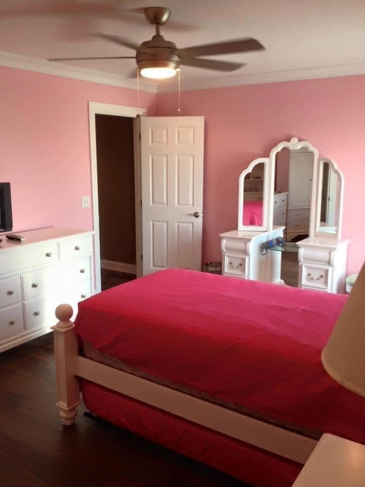 Pink bedroom with white furniture, dark wood floor, ceiling fan, and a pink bed.