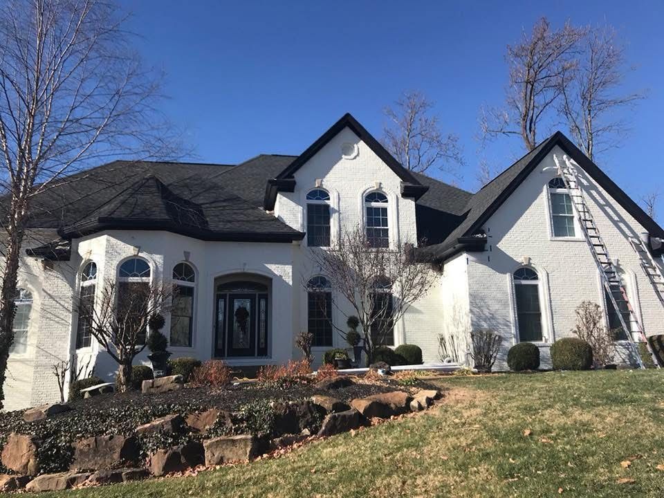 White house with black trim and a dark roof, ladder propped on the side.