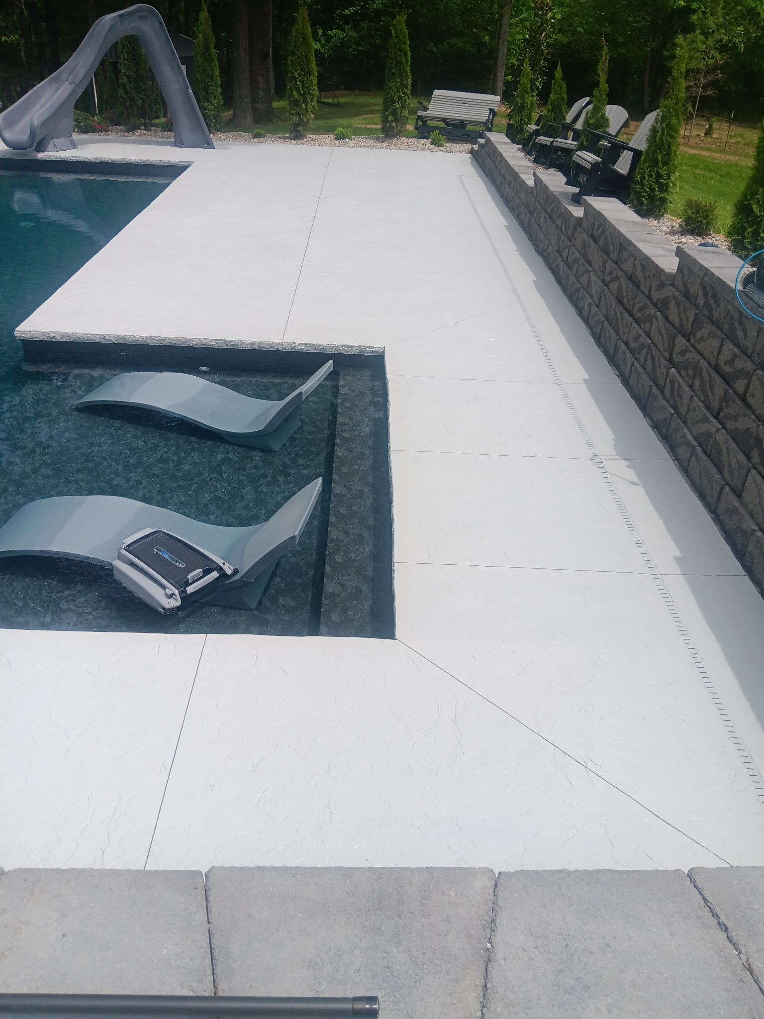 Poolside patio with built-in lounge chairs, a slide, and a stone retaining wall.