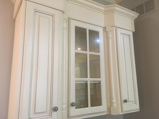 Cream-colored kitchen cabinets with decorative molding and glass-paned door; part of a kitchen.
