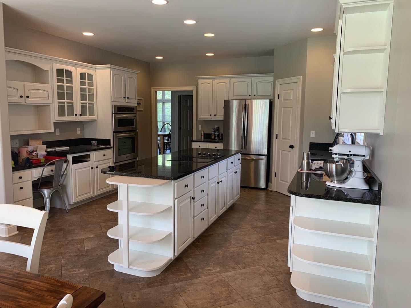 White kitchen with island, black countertops, stainless steel appliances, and shelving.